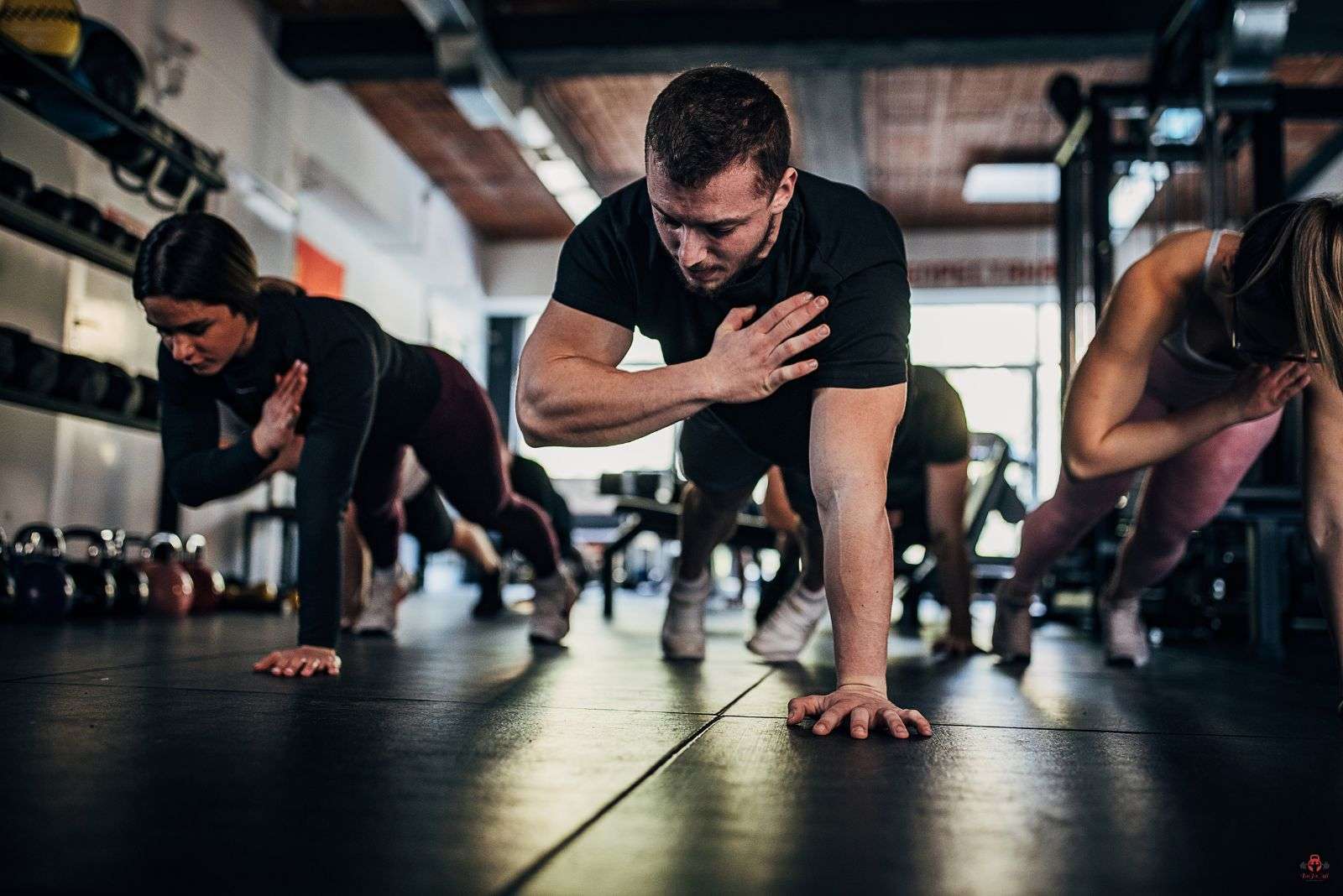 Skupina lidí v gymu, kteří cvičí s vlastní váhou.
